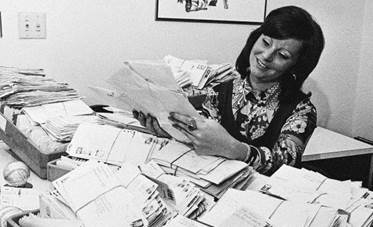 A woman sitting at a desk that's covered with huge piles of unopened letters.