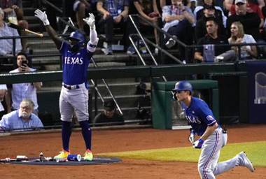 Corey Seager runs out of the batters box after a home run. In the background, Adolis García drops his bat and throws his arms in the air.