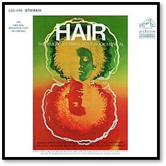 Psychedelic green and yellow colorized photo-negative of a man's face with a bushy "afro", reflected below in red and yellow.